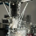 Dynamic close-up of CNC machine with coolant splashing during metalwork operation.